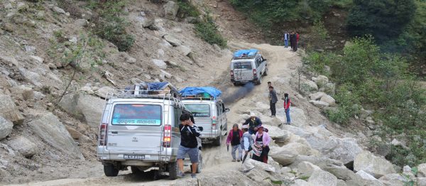 Jeep driving on winding mountain road surrounded by green hills with blue sky, carrying climbers for Manaslu expedition start.